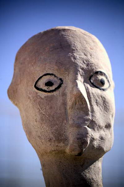 Close view of a rounded sculpted head with prominent eyes outlined in black.
