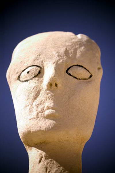 A pale sculpted face tilted upwards, with almond-shaped eyes drawn in black.