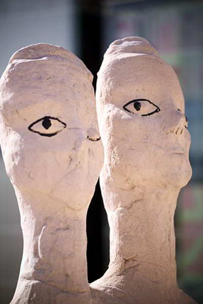 Two elongated sculpted heads side by side, their eyes outlined in black.