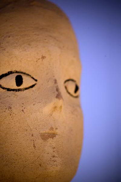 Very close view of a sculpted face, a black drawn eye and part of the nose.