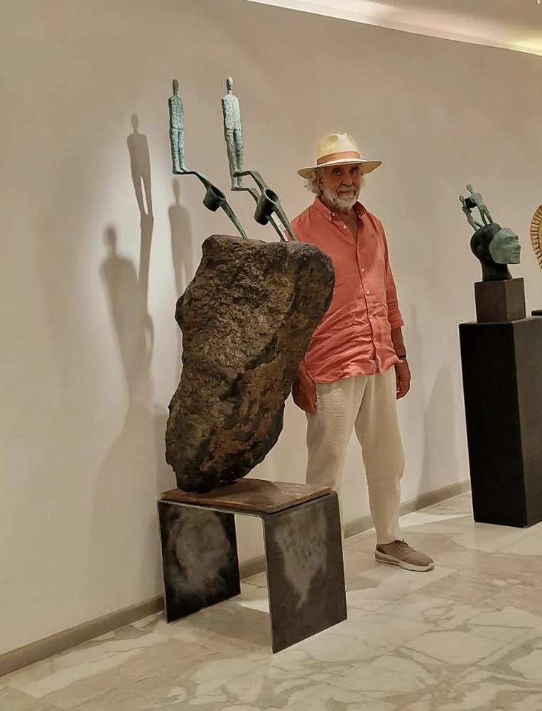 A man beside a basalt boulder carrying two small bronze figures on stems.
