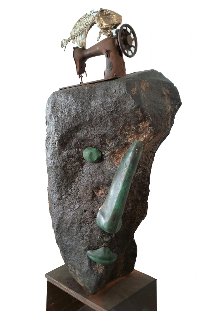 A stone face topped by a sewing machine and a fish.