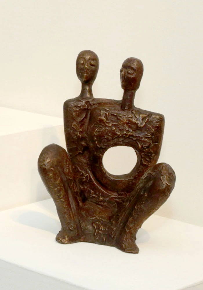 A seated two-headed figure with a circular opening in the torso.
