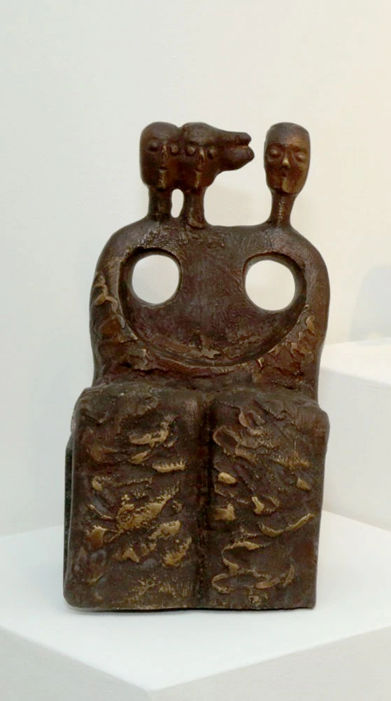 A seated form with multiple heads and two circular openings.