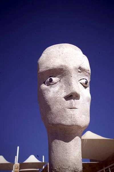 A pale sculpted head lit by the sun, against a deep blue sky.