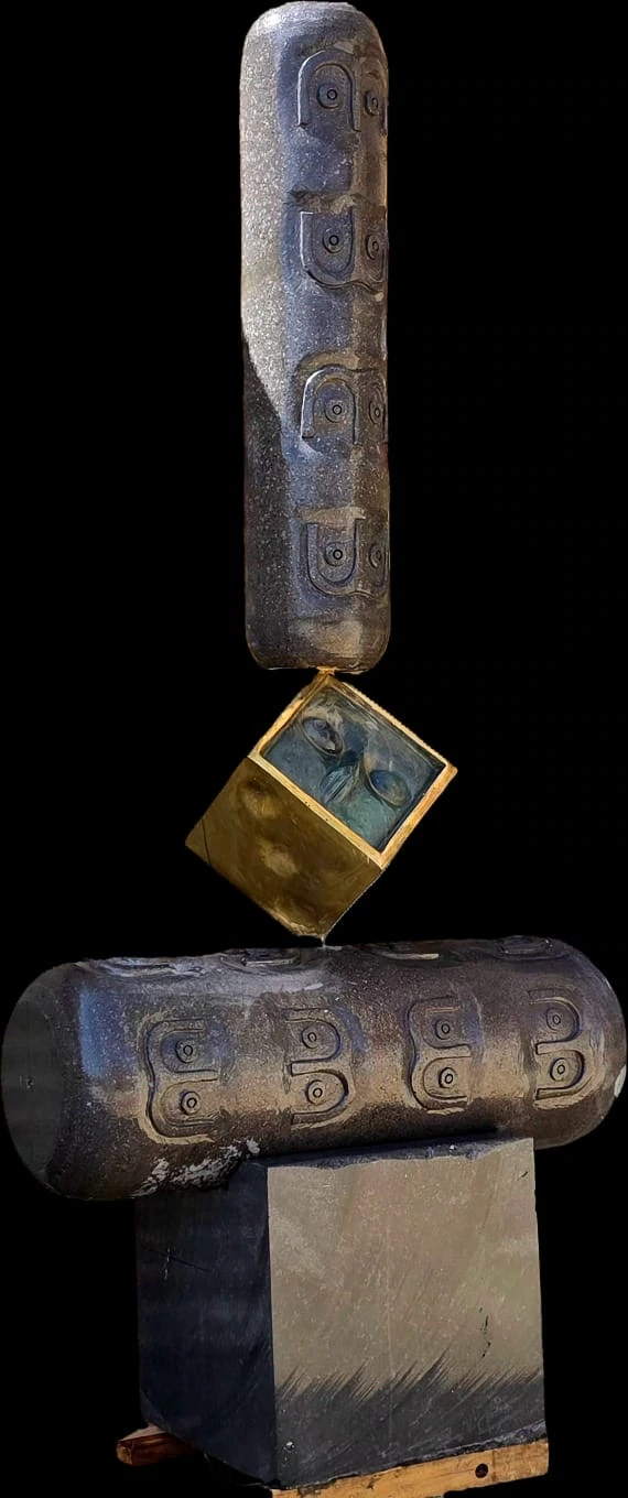Basalt cylinders carved with paired faces, balanced around a golden bronze cube against a dark background.