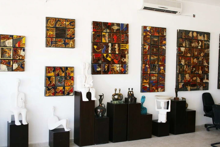 Gallery interior with orange-toned ceramic wall panels and pale and bronze figures on dark plinths.