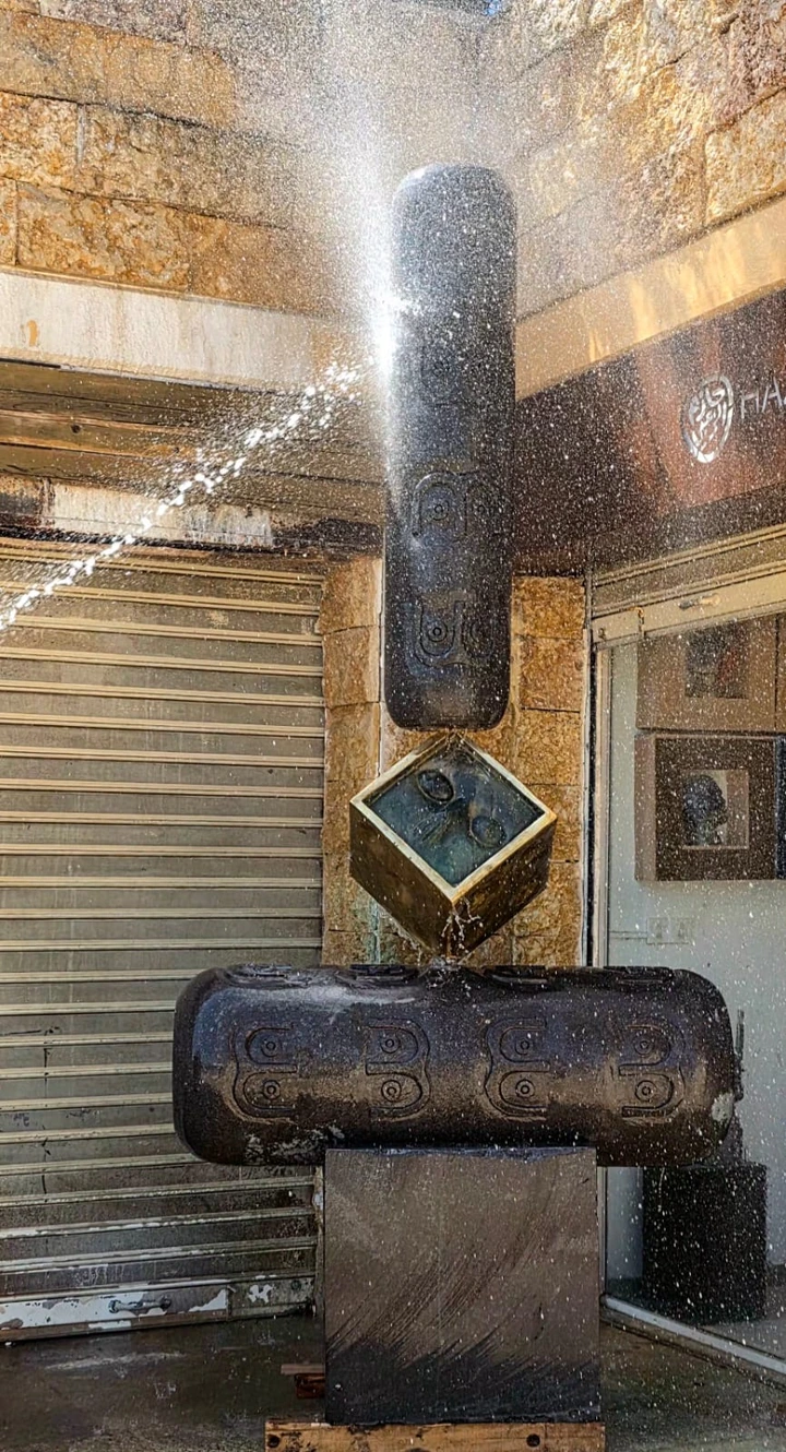 Closer view of water falling over the carved basalt cylinders and the tilted bronze cube.