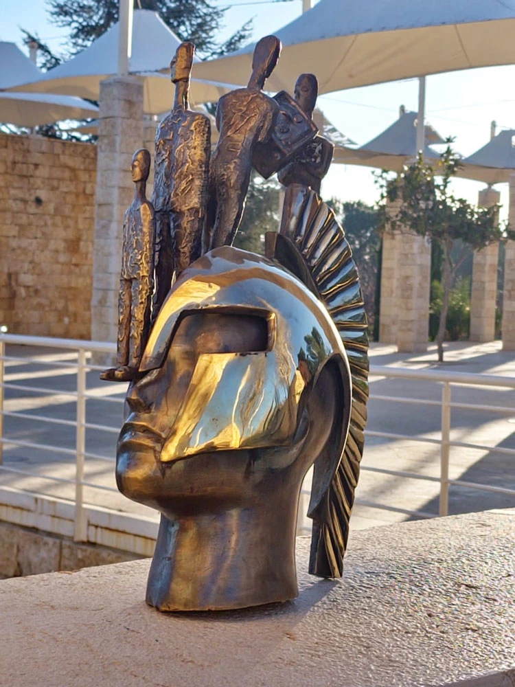 A helmeted head with standing figures, photographed outdoors.