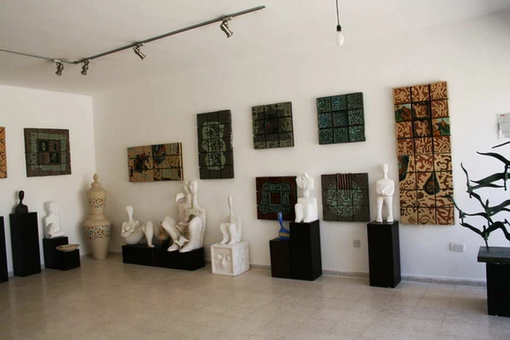 Wide view of the gallery with ceramic vessels, pale figures and green and ochre wall panels.