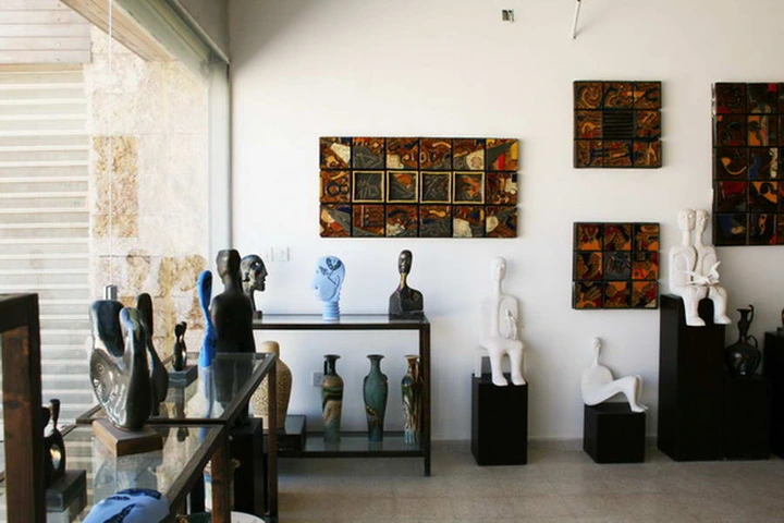 Sculpted heads on a glass display table, with seated figures and tiled panels along the gallery wall.