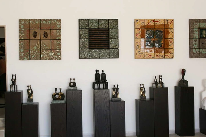 A row of small bronze figures on tall dark plinths beneath square ceramic wall compositions.