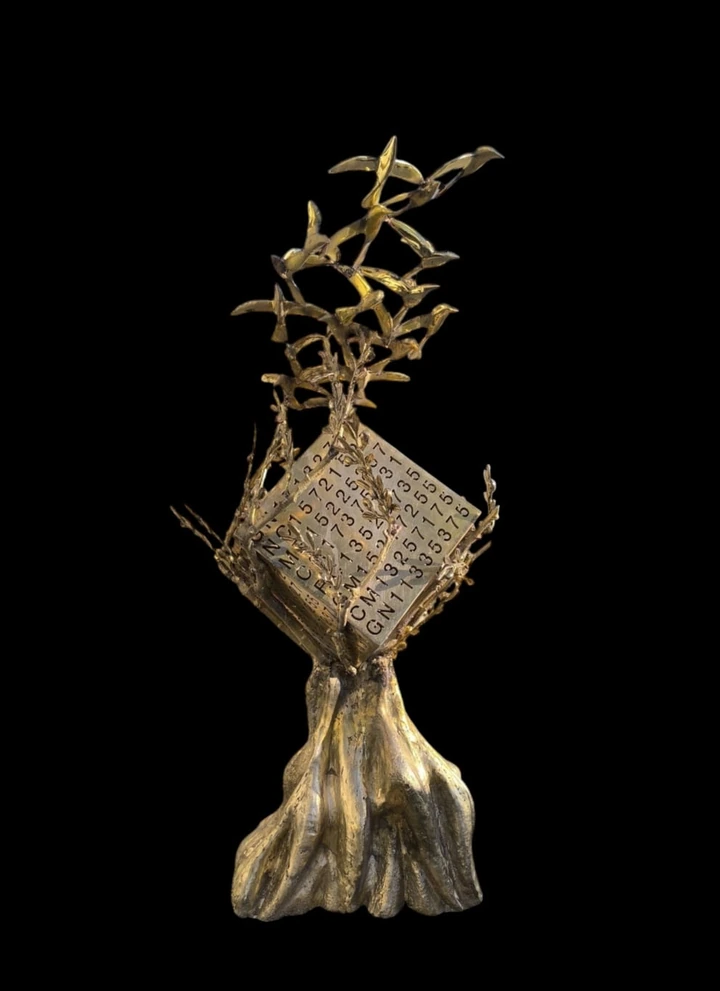 Front view of a bronze tree, inscribed cube and ascending birds against a black background.