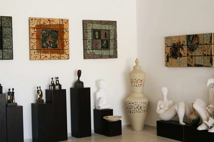 Gallery corner where small bronze figures stand beside a tall cream vessel and pale reclining sculptures.