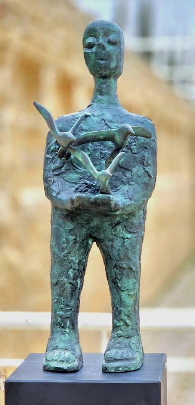 Front view of a green-patinated standing figure carrying three birds across its chest and hands.