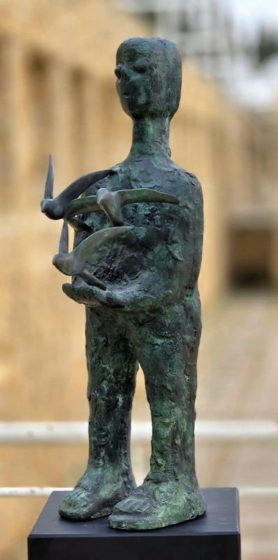 Three-quarter view of a green-patinated figure with birds extending from its cupped hands.