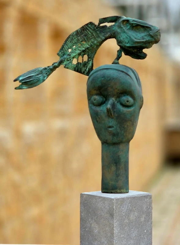 A bronze head with a large pierced fish arcing over it instead of birds.