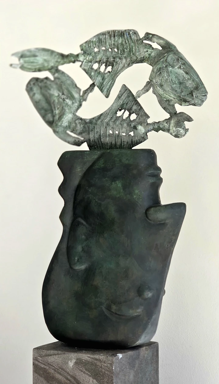 A sculpted head with pierced fish forms above it; a softly focused view.