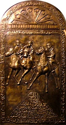 A cast bronze plaque of three horsemen at the gallop, framed above and below by bands of Arabic inscription.