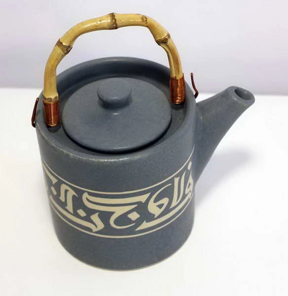 A grey teapot with a bamboo handle, a band of pale Kufic calligraphy round the body.