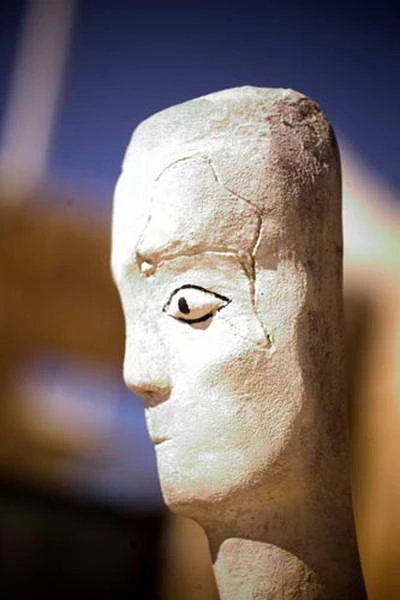 A plaster head in profile with a single drawn eye, outdoors.