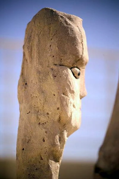 A tall plaster head in profile, eye drawn, outdoors.