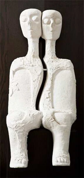 Two pale sculpted figures joined side by side, with long necks and outlined eyes.