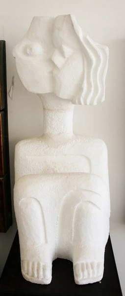 A seated white plaster figure with a stylised head and waved hair.