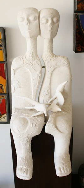 Two seated white plaster figures with a small bird held between their hands.