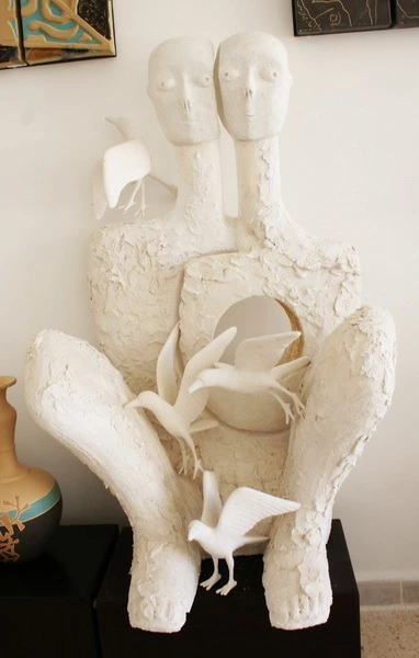 Two seated white plaster figures with birds rising from an opening in the chest.
