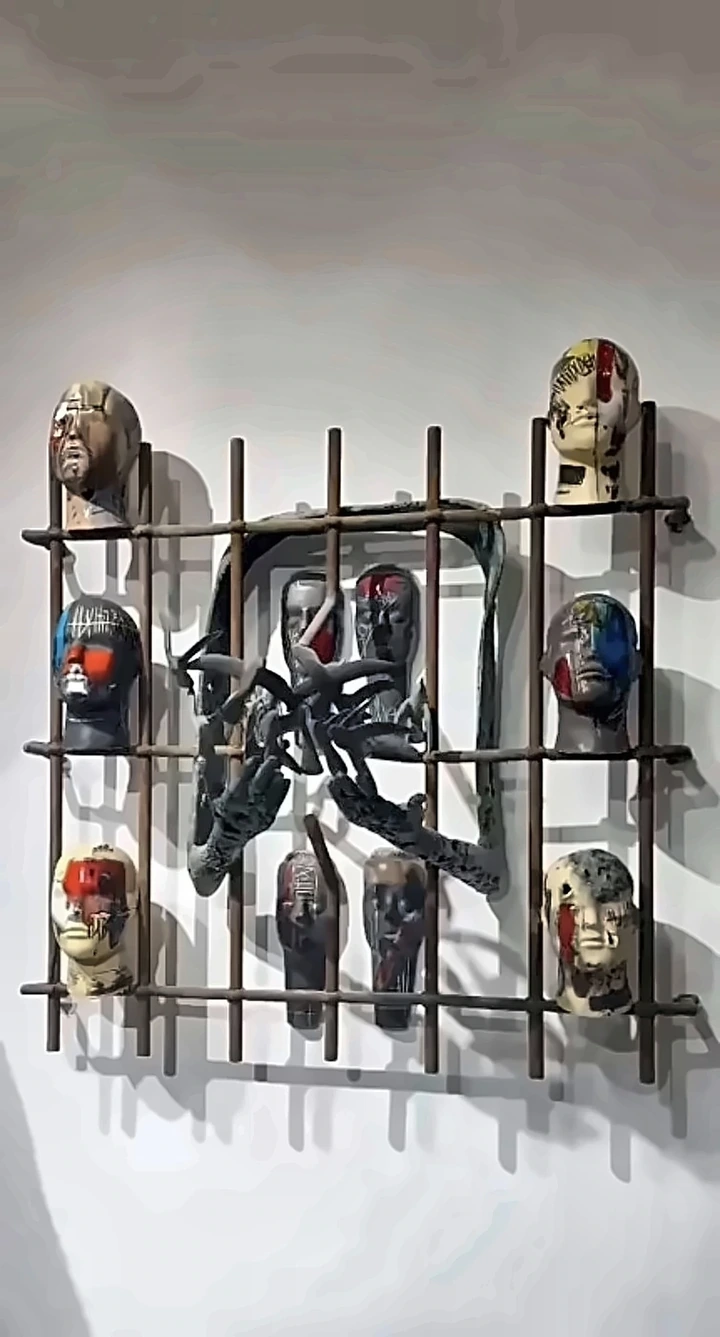 Painted ceramic heads held in a welded iron grid on a wall.