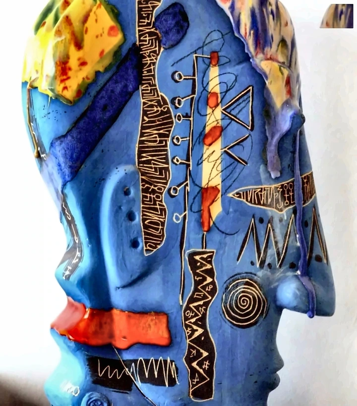 Blue-glazed ceramic head in profile, with incised lettering, spiral motifs and red and yellow accents.