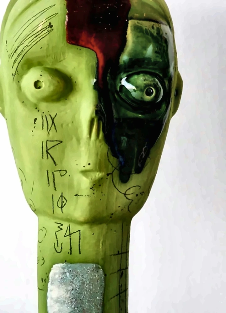 A green-glazed ceramic head split by a band of red and black glaze.