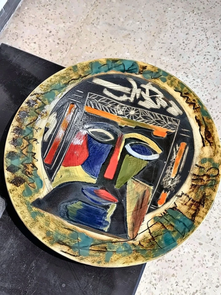 Circular ceramic plate with a stylised face, red nose and blue and yellow glaze.