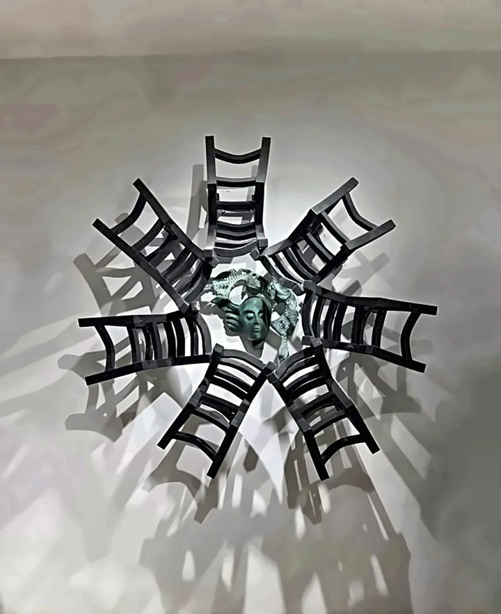 Chairs arranged in a ring around a bronze head, casting long shadows.