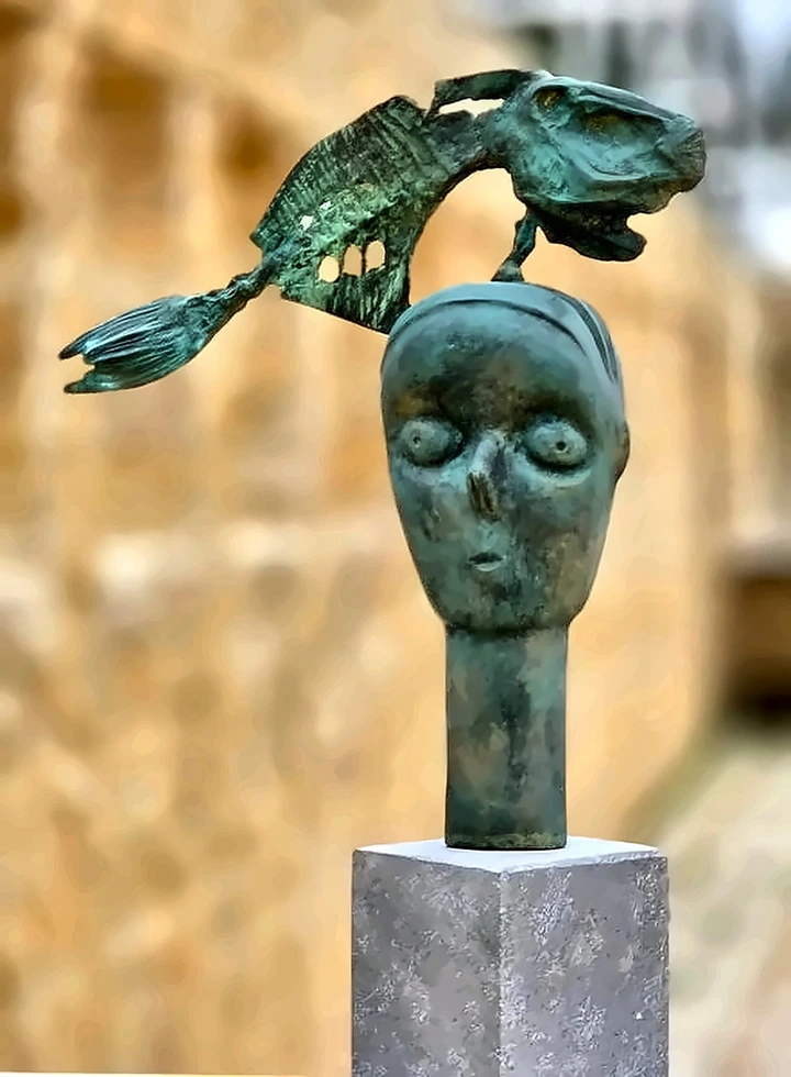 A bronze head with a large pierced fish arcing over it instead of birds.