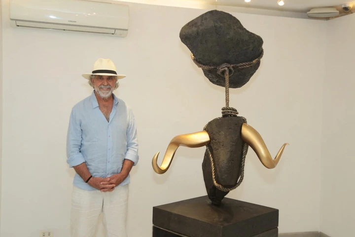 A man in a straw hat beside a bull: basalt and gilded bronze horns, roped, on a black plinth.
