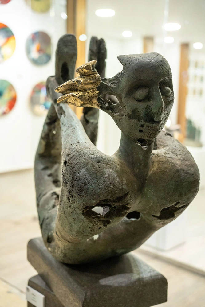 A reclining bronze figure with raised arms, the metal eaten through, a small cluster of gilded birds at the head.