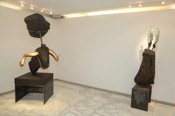 The suspended stone with gilded horns, beside two figures above a boulder.