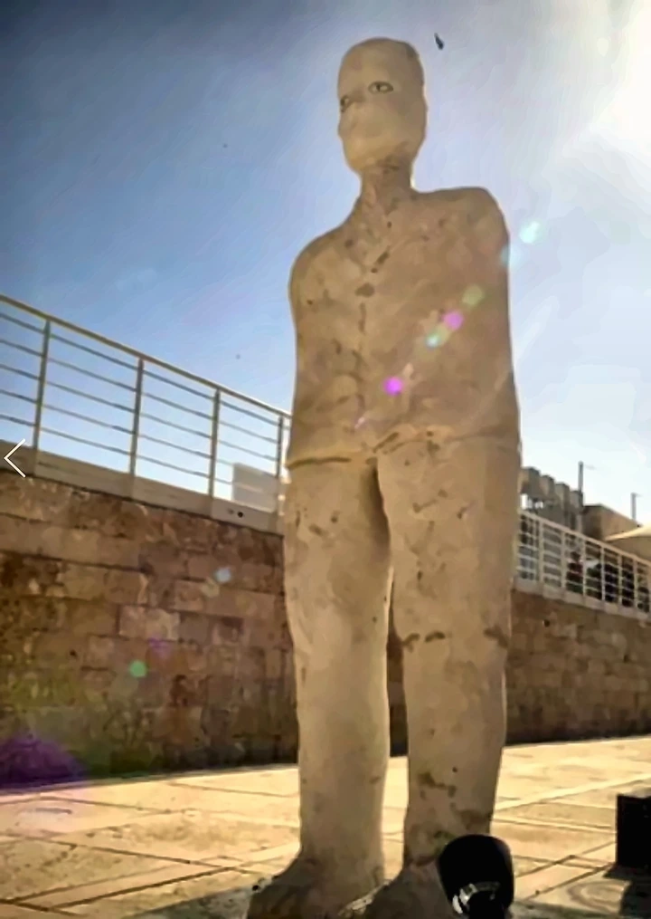 Standing limestone figure on a dark plinth in an outdoor courtyard.