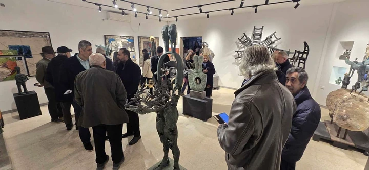 A crowded gallery hall on opening night with bronze figures among the guests.