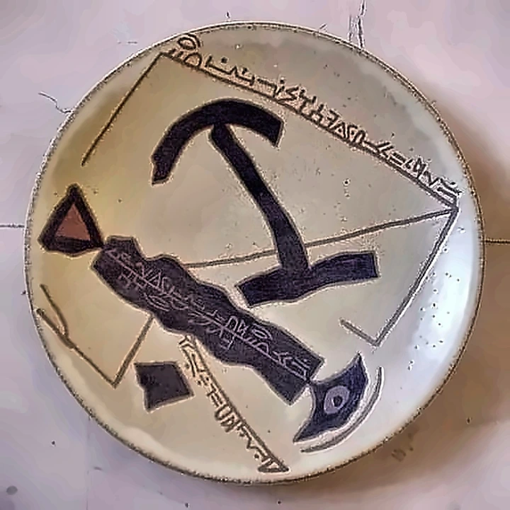 A cream plate with a large black anchor form and lines of script running along the rim and through the centre.