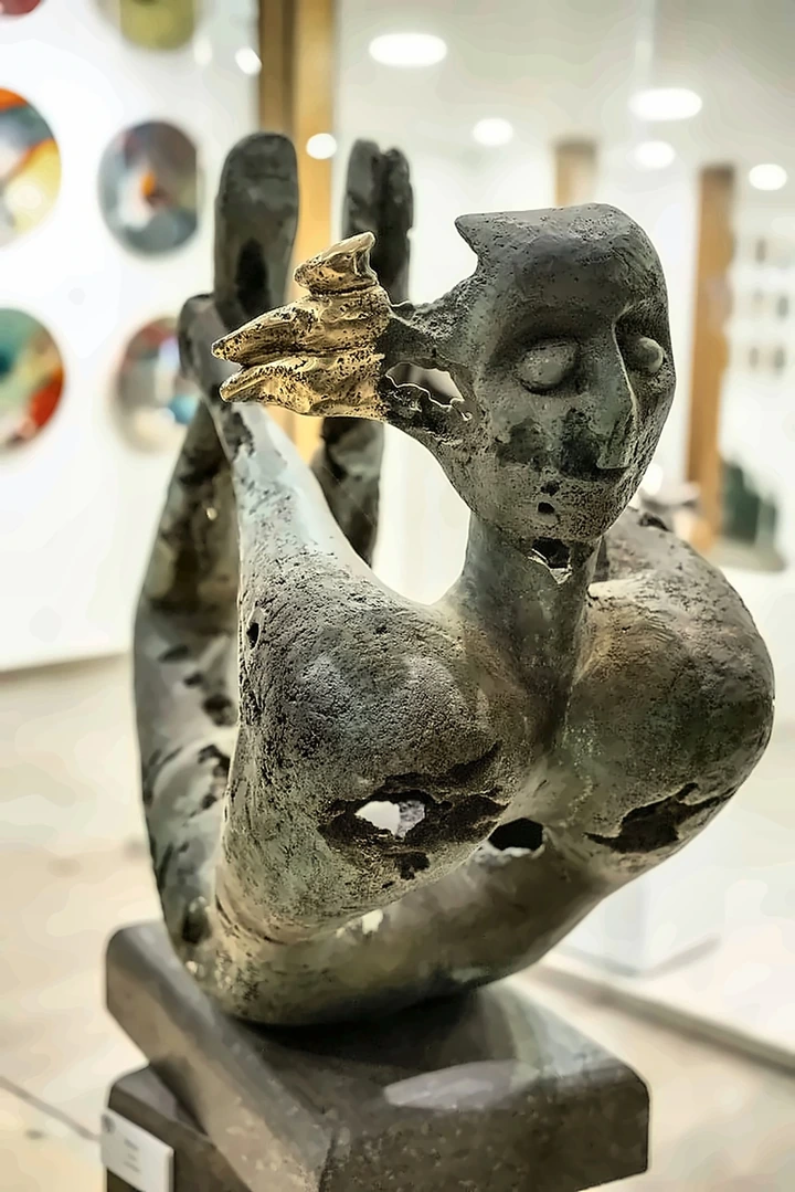 A reclining bronze figure with raised arms, the metal eaten through, a small cluster of gilded birds at the head.