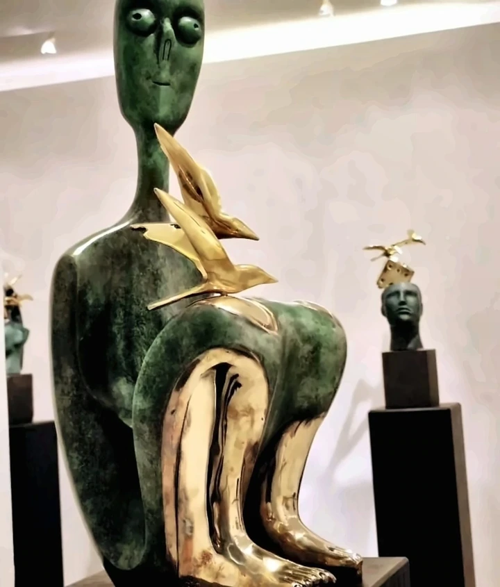 Seated turquoise-patinated figure with polished gold-coloured bands along the neck, chest and lap.