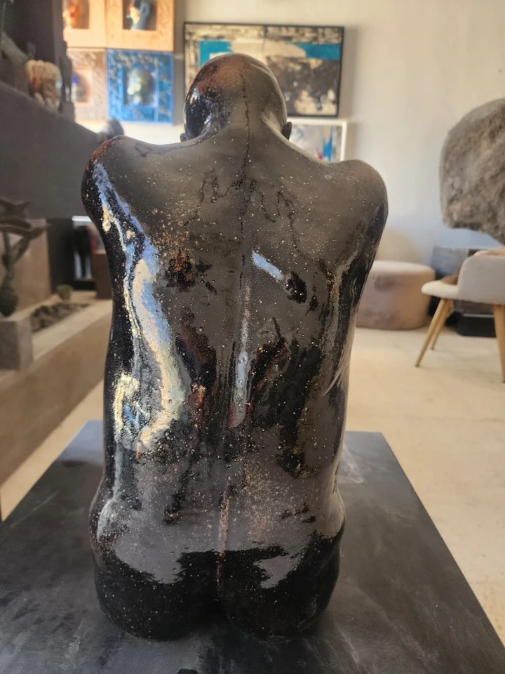 The back of the seated figure, black glaze pooling over red clay.