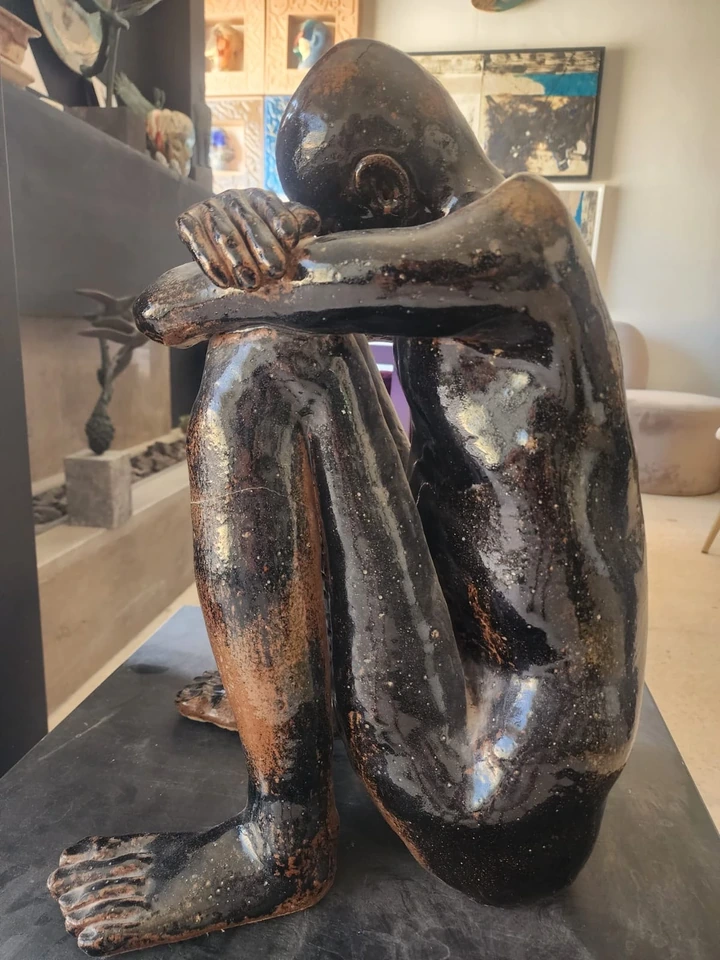 Close view of the hands resting on the knees, glaze worn to the clay at the edges.