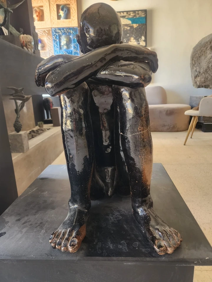 The seated stoneware figure from the front, feet flat, arms crossed over the knees.