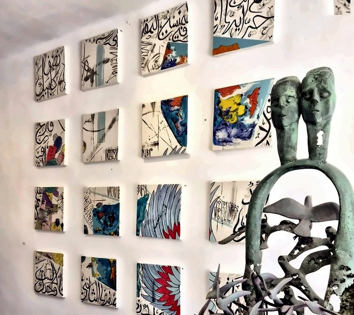 Grid of small ceramic wall panels behind a bronze figure in the gallery.