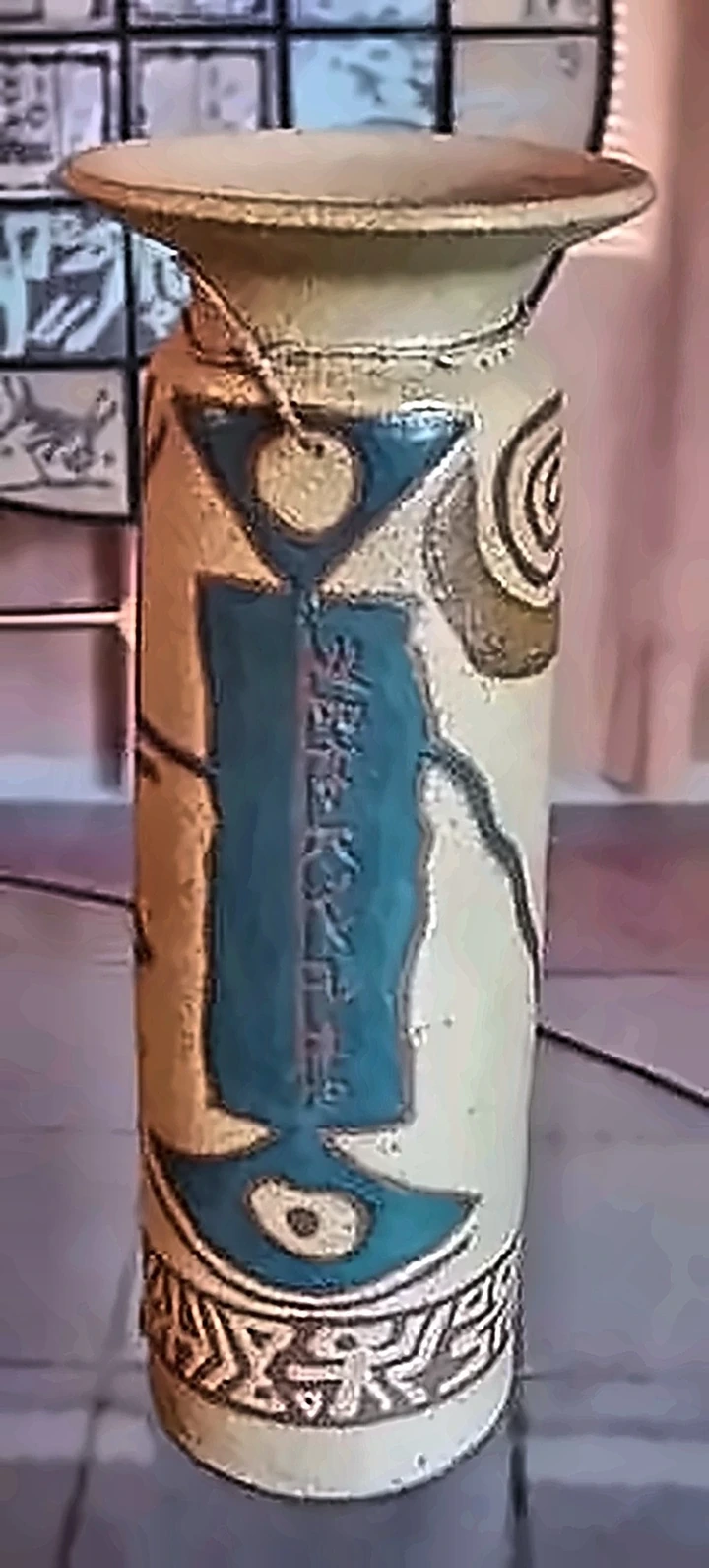 A cylindrical vase, a turquoise panel of script down its face over pale stoneware.