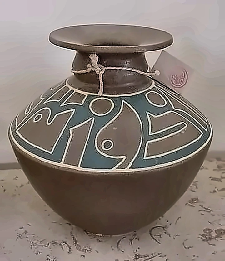 A dark round-bellied jar with a wide flared neck, its shoulder banded in turquoise with pale incised figures.